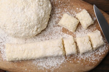 Making lazy dumplings. Wooden board with raw dough, flour and knife on table, flat lay