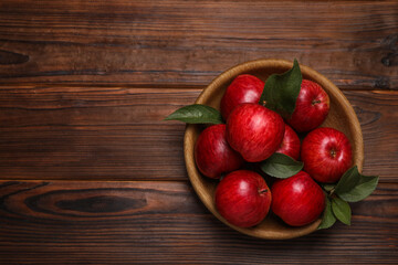 Ripe red apples and green leaves in bowl on wooden table, top view. Space for text