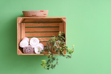 Wooden box with towels and plant on green wall