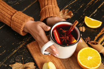 Woman holding cup of hot mulled wine with apple and orange on black wooden background