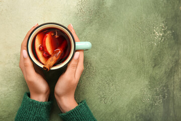 Woman holding cup of hot mulled wine with apple and pomegranate on grunge background