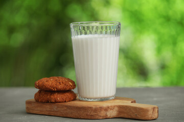 Wooden board with glass of fresh milk and sweet cookies on grey table outdoors