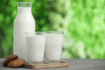 Glasses and bottle of fresh milk on grey table outdoors
