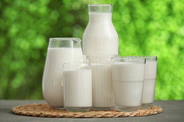 Glasses and bottle of fresh milk on grey table outdoors