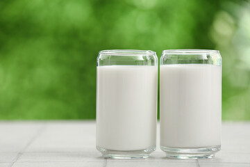 Glasses of fresh milk on white tile table outdoors