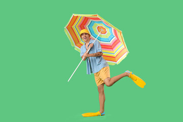 Happy young man in flippers with umbrella on green background