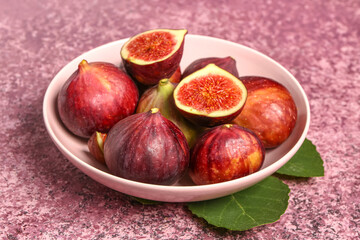 Plate with ripe fresh figs and plant leaves on grunge pink background