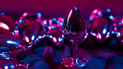 Lots of metal anal plugs in neon pink purple light. 