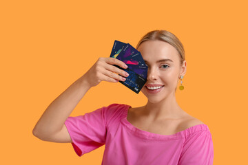 Pretty young woman with credit cards on orange background