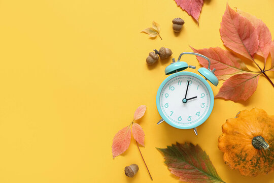 Alarm clock with autumn leaves and pumpkin on orange background
