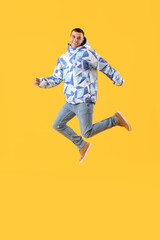 Fototapeta na wymiar Young man in warm jacket jumping on yellow background
