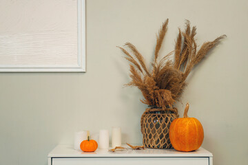 Vase with pampas grass, pumpkins and candles on commode in room