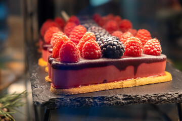 Sweet pastries with berries. Showcase in a candy store. Glass stand with cake eclairs and tartlets....