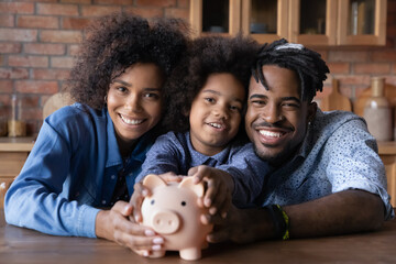 Head shot portrait happy African American family holding piggy bank, looking at camera, smiling...