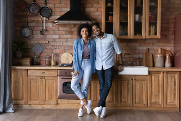 Portrait smiling African American woman and man standing in modern kitchen, looking at camera,...