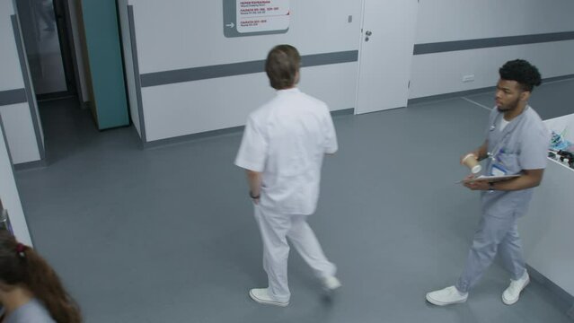 Busy hospital corridor: Diverse doctors, multiethnic medics, nurses, surgeons and patients walking. Female physician calls elevator. Medical staff work in modern clinic or medical facility. High angle