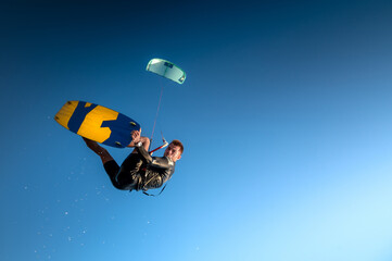 Sports kitesurfer in the air doing a trick with a wakeboard, rider in a wetsuit on a clear blue sky...