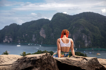 Beautiful girl with orange hair on a high mountain overlooking the sea. Beautiful bay. Tropical nature.