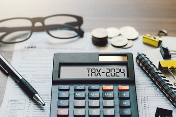 Word Tax 2024 on the calculator. Business and tax concept.Calculator, coins, book, tax form, and pen on table.Tax deduction planning.Financial research, government taxes, and calculation tax return - obrazy, fototapety, plakaty