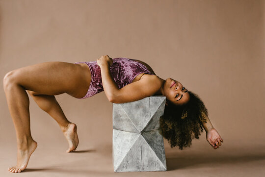 Female multi racial dancer with curly hair does back bend on stool