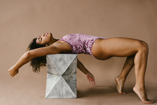 Dancer does body figure pose on cement block in pink leotard