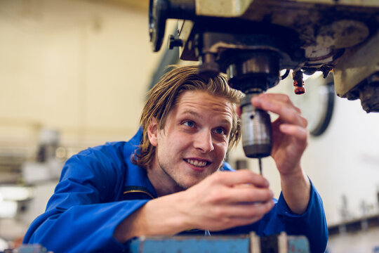 Happy young man standing at drilling machine and repairing in factory