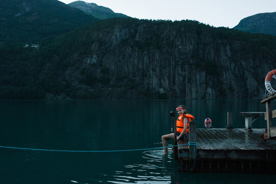 girl sat on a dock with a life vest waiting to swim in Norway