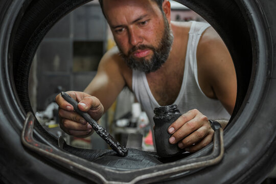 man applies glue with a brush on a tire to patch it in his garage