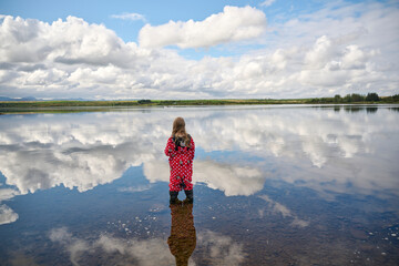 Unrecognizable kid contemplating cloudy sky while standing in lake