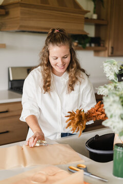 A woman arranging a bouquet of fall flowers on her kitchen count