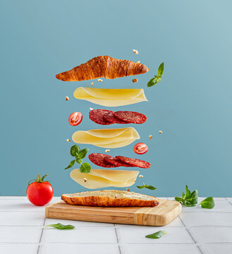 Sandwich with flying ingredients. Croissant with cheese and salami.