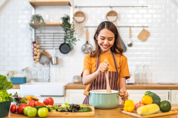 Young woman standing near stove and cooking, housewife, meal, chef, food.Happy woman looking and smelling tasting fresh delicious from soup in a pot with steam at white interior kitchen