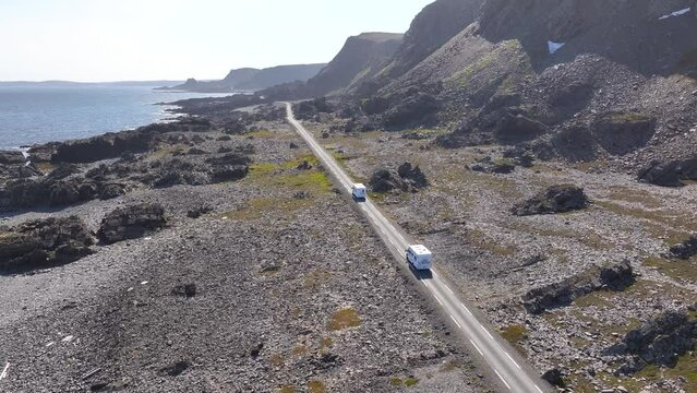 Two camper vans traveling on a beautiful road from Hamningberg in the north of Norway under the summer sun