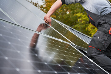 Man technician mounting photovoltaic solar panels on roof of house. Close up view of engineer installing solar module system with help of hex key. Concept of alternative, renewable energy.