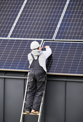 Man mounter mounting photovoltaic solar panels on roof of house. Engineer in helmet installing...