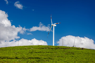 Windmill turbine with a blue sky and green field