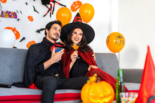 Couple having fun holding pumpkins and wearing dressed carnival halloween costumes and makeup posing with bats and balloons on background at the halloween party.Halloween holiday celebration concept