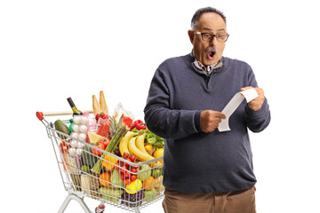 Shocked mature male customer with a shopping cart looking at a bill