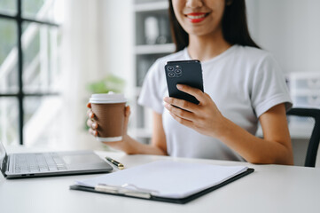 Asian Woman using smart phone for mobile payments online shopping, omni channel, sitting on table,...