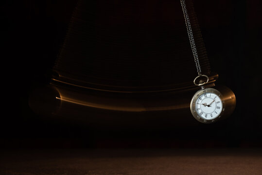 Hypnosis session. Vintage pocket watch with chain swinging over surface on dark background among faded clock faces, magic motion effect