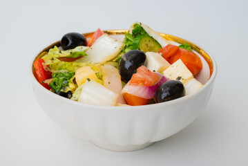 Greek salad of fresh cucumber, tomato, sweet pepper, lettuce, red onion, feta cheese and olives with olive oil on a white background.