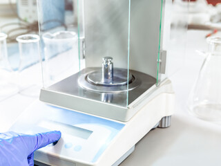 A operator's hand is holding steel calibration weight to place on the analytical balance. Concept of quality control in a laboratory.