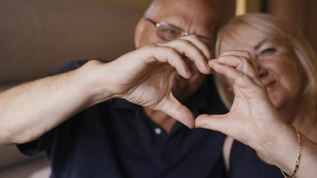 An elderly couple shows a heart with their hands as a sign of love for their loved ones. Close-up.
