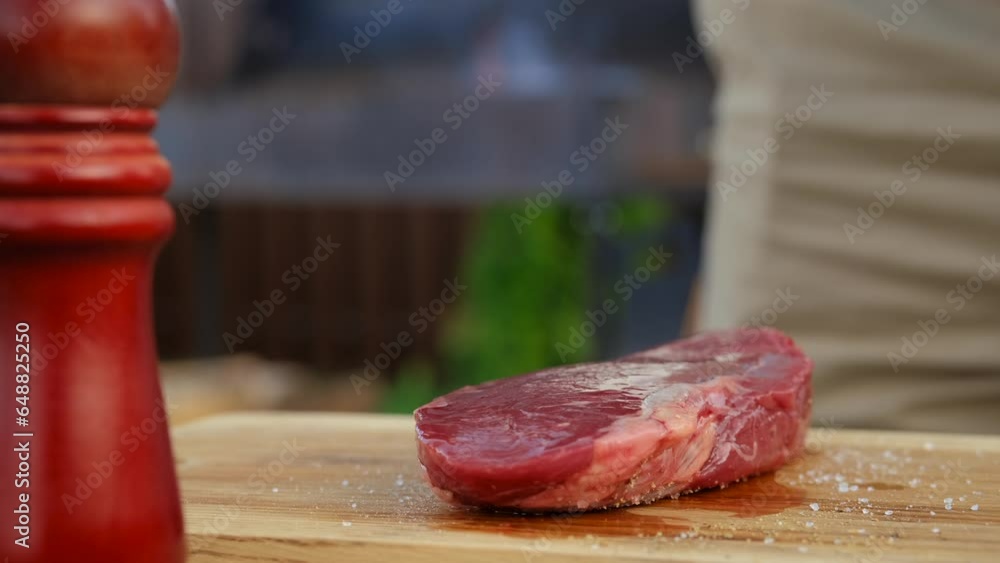 Wall mural unrecognizable man seasoning raw beef steak with salt and pepper