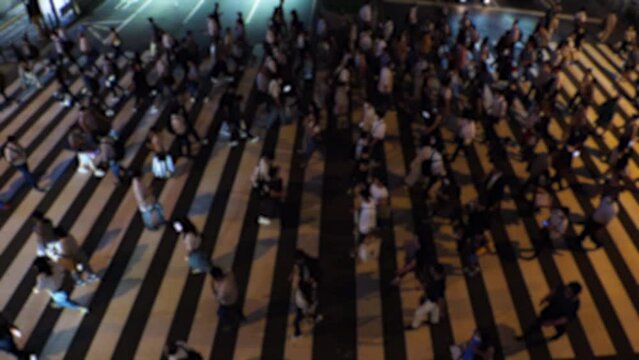 OSAKA, JAPAN - JULY 2023 : Aerial view of unidentified crowd of people walking at the zebra crossing at night. Slow motion shot. Japanese people and city lifestyle concept video.