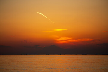 夕焼けに浮かび上がる富士山のシルエットと飛行機雲と茜雲