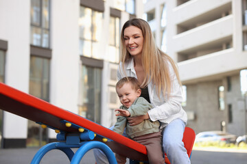 Happy nanny with cute little boy on seesaw outdoors