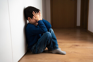 Upset problem child with head in hands sitting on floor concept for bullying, depression stress or...