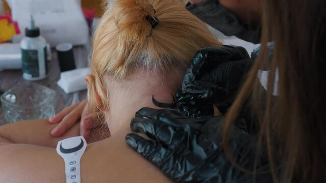 Tattooing process. Close up. Tattoo machine studio female artist. Black gloves.