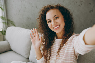 Close up young fun woman wear casual clothes sits on grey sofa couch do selfie shot pov on mobile cell phone waving hand stay at home hotel flat rest relax spend free spare time in living room indoor.